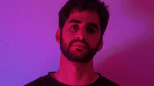 A man with a beard standing in front of a purple light.