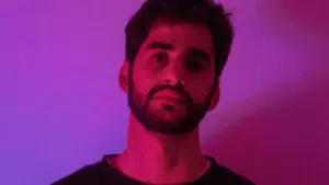 A man with a beard standing in front of a purple light.