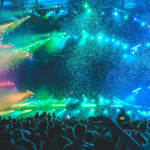 A crowd of people at a concert with colorful lights and confetti.