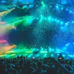 A crowd of people at a concert with colorful lights and confetti.