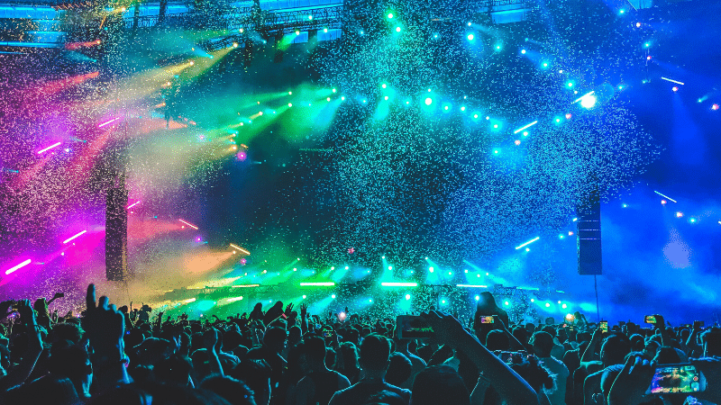 A crowd of people at a concert with colorful lights and confetti.