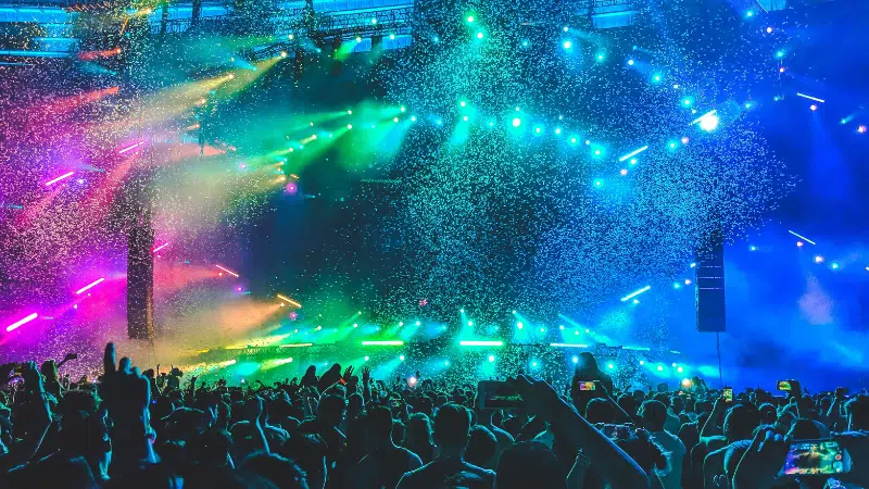 A crowd of people at a concert with colorful lights and confetti.