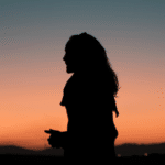 A silhouette of a woman standing in front of a sunset.