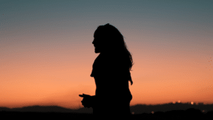 A silhouette of a woman standing in front of a sunset.