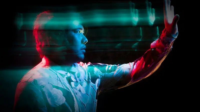 A man is holding his hand up in front of a dark background.