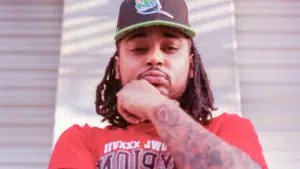 A man with dreadlocks and a hat leaning against a wall.