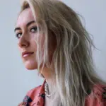 A woman with long blonde hair is staring off into the distance.