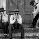 Three men in suits and hats sitting on steps.