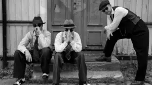 Three men in suits and hats sitting on steps.