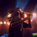 A man with long hair singing into a microphone.