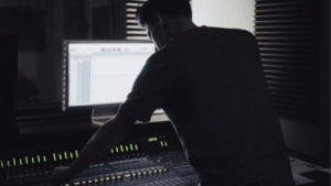 A man working on a mixing console in a dark room, planning.