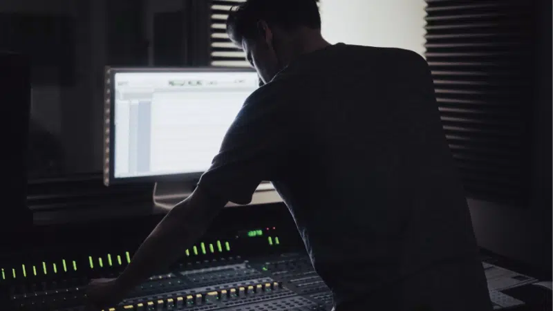 A man working on a mixing console in a dark room, planning.