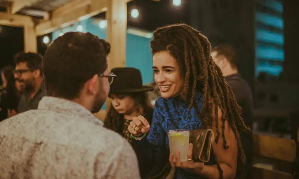 A woman with dreadlocks engaging in a conversation with a man at a community party.