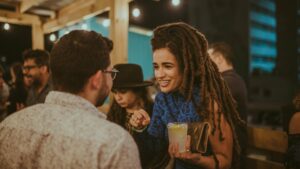A woman with dreadlocks engaging in a conversation with a man at a community party.