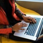 Person in a camouflage jacket using a laptop on a yellow chair, reminiscent of musicians during coronavirus finding creative ways to connect with their audience.