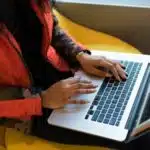 Person in a camouflage jacket using a laptop on a yellow chair, reminiscent of musicians during coronavirus finding creative ways to connect with their audience.