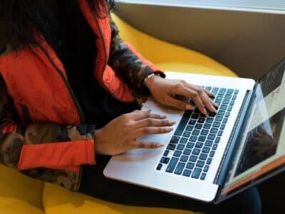 Person in a camouflage jacket using a laptop on a yellow chair, reminiscent of musicians during coronavirus finding creative ways to connect with their audience.