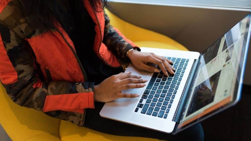 Person in a camouflage jacket using a laptop on a yellow chair, reminiscent of musicians during coronavirus finding creative ways to connect with their audience.