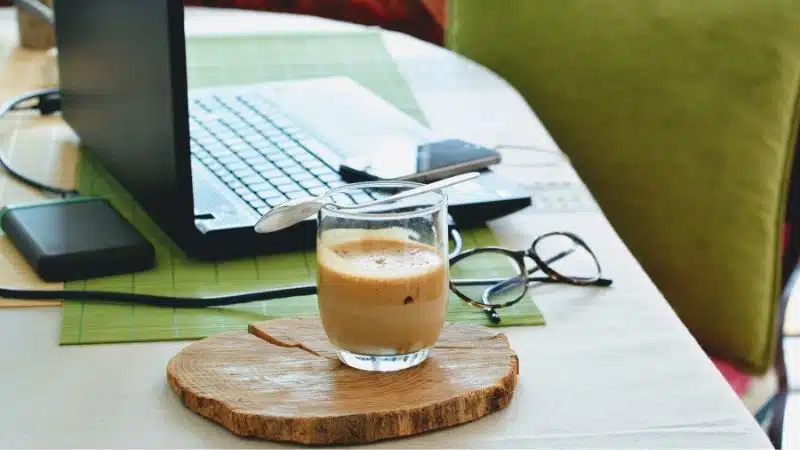 Managers working during quarantine with a cup of coffee on a wooden board next to a laptop.