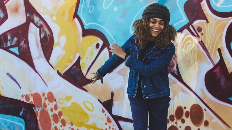 A woman smiling in front of a wall with graffiti for press photos.