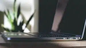 A laptop sits on a wooden table next to a plant, offering potential to earn money through YouTube.