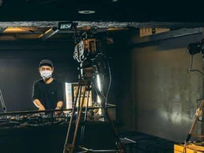 A dj live streaming in front of a camera in a dark room.