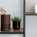 A person is pointing to an amazon echo speaker on a shelf, showcasing its voice capabilities.