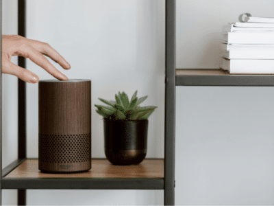 A person is pointing to an amazon echo speaker on a shelf, showcasing its voice capabilities.