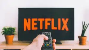 A person holding a Netflix remote in front of a tv, watching movies.