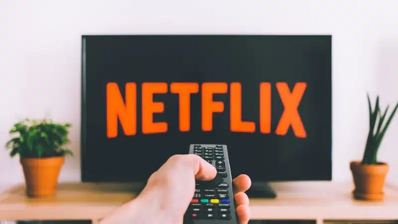 A person holding a Netflix remote in front of a tv, watching movies.