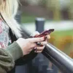 A woman using a cell phone while standing on a railing.