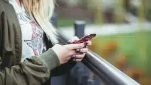 A woman using a cell phone while standing on a railing.