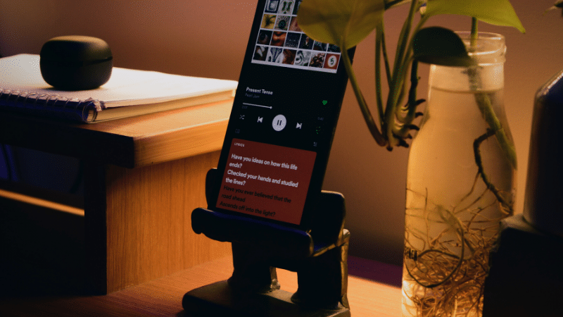 A phone is sitting on a table next to a plant, providing the perfect ambiance for enjoying work from home playlists.