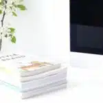 A stack of books on a desk next to a computer.