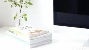 A stack of books on a desk next to a computer.