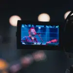 A video camera capturing a man singing, aiming to sell more merch.