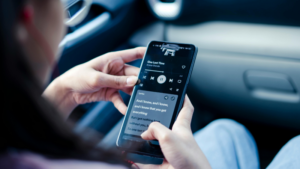 Person holding a smartphone in a car, playing music and viewing lyrics on Spotify displayed on the screen.
