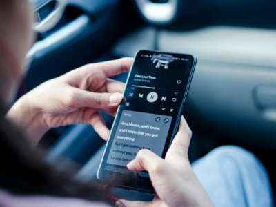 Person holding a smartphone in a car, playing music and viewing lyrics on Spotify displayed on the screen.