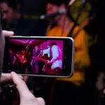 A person using a cell phone to record a band performance for editing with video editing apps.