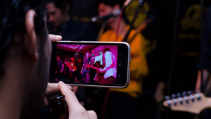 A person using a cell phone to record a band performance for editing with video editing apps.