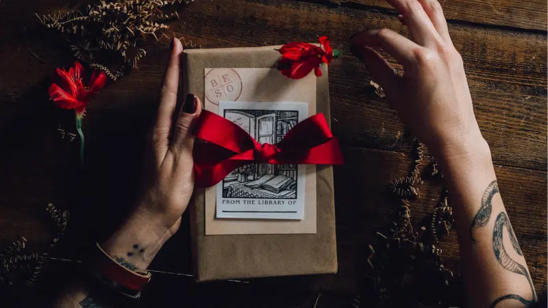 A woman's hand holding a gift box with red roses, offering holiday marketing tips.