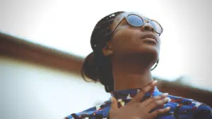 A woman wearing sunglasses, mesmerized by the excellence of black music playing, looks up at the sky.