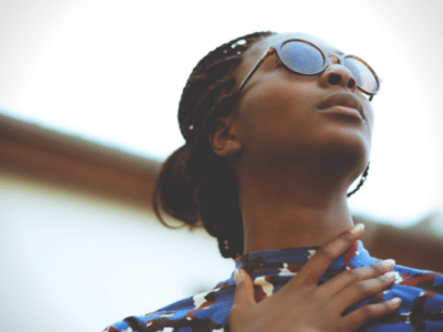 A woman wearing sunglasses, mesmerized by the excellence of black music playing, looks up at the sky.