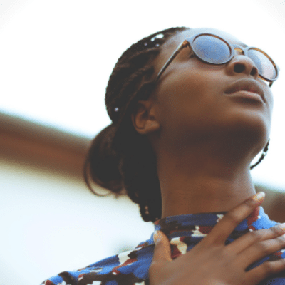 A woman wearing sunglasses, mesmerized by the excellence of black music playing, looks up at the sky.