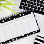 A black and white polka dot planner, perfect for goal setting, is seen on a desk alongside a laptop and a plant.