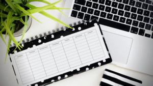 A black and white polka dot planner, perfect for goal setting, is seen on a desk alongside a laptop and a plant.