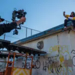 A man capturing a music video on top of a building with graffiti.