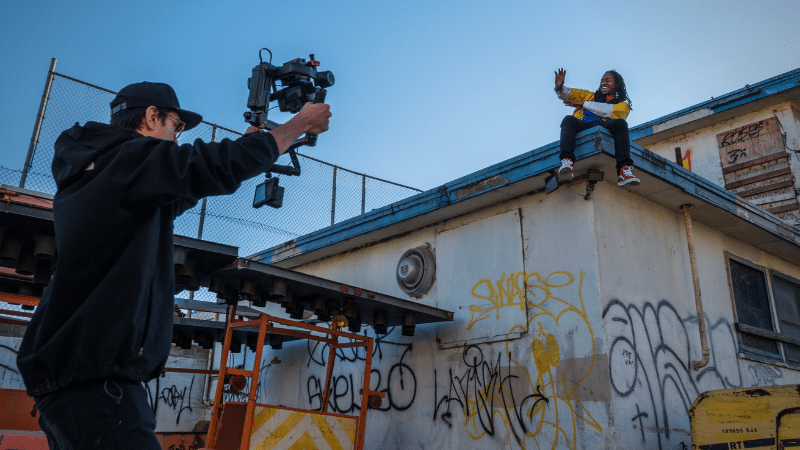 A man capturing a music video on top of a building with graffiti.