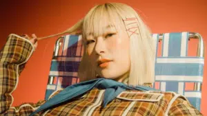 A AAPI woman in a plaid shirt is sitting on a chair.