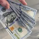 A musician holding a stack of dollar bills in front of a staircase, showcasing their success in money management.